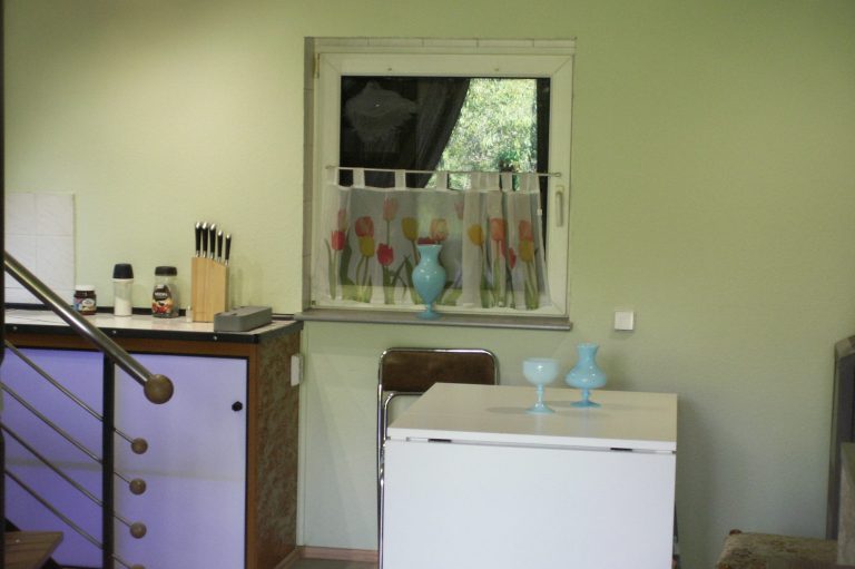 Essbereich Küche mit grünem Wandfarbton, Fenster mit Vorhang und Geschirr auf der Theke.