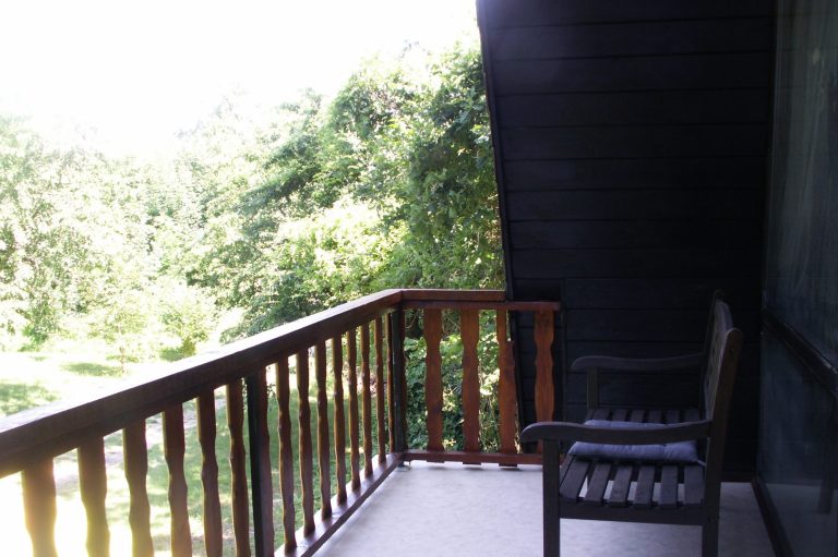 Balkon Ein Balkon mit Holzgeländer und einem Stuhl, umgeben von grüner Vegetation.
