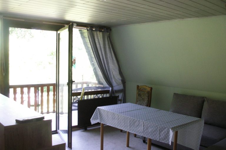 Stube Heller Wohnraum mit Tisch, Stühlen und einer offenen Balkontür.
