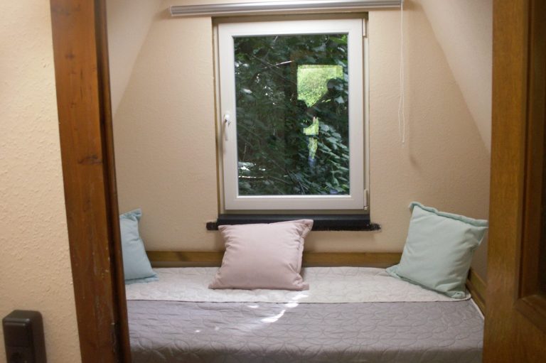 Schlafzimmer 2 Gemütliche Bett mit Kissen neben einem Fenster mit Blick ins Grüne.